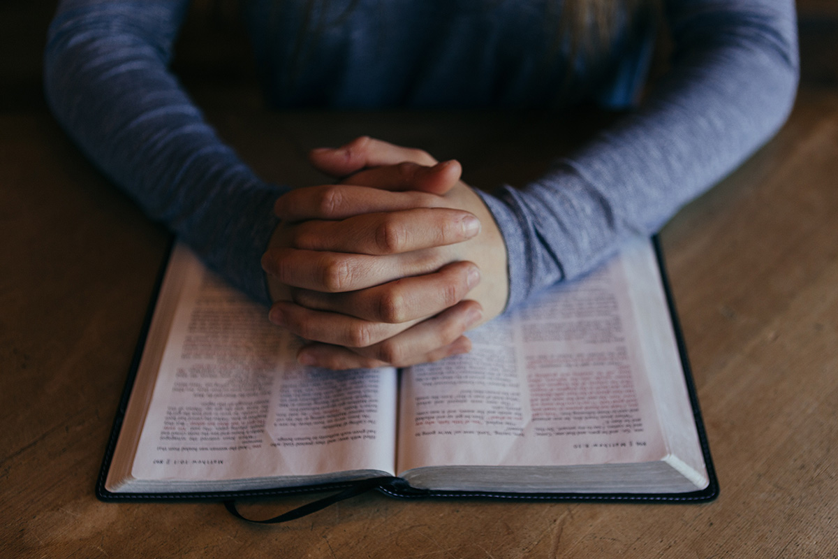 man praying with hands clasped on open Bible